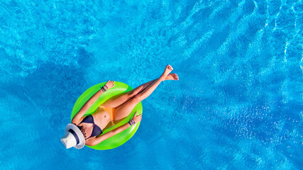 Beautiful woman in hat in swimming pool aerial view from above, young girl relaxes and has fun on inflatable ring in water on vacation
