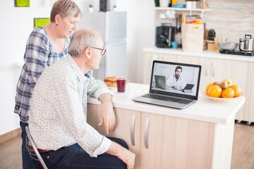 Senior patients on video conference with doctor using laptop in kitchen. Online health consultation...