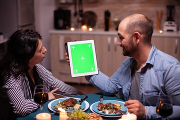 Couple using tablet pc with green template during festive dinner. Husband and wife looking at green...