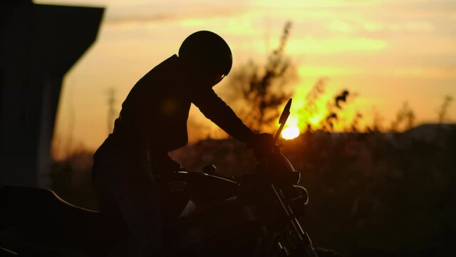 Close-up Biker Man Walking Through Parking to his Standing Motorcycle in City. Concept Motorcyclist and Motorbike. Person Driver Starts and Sit on Bike in Urban Lifestyle. Cinematic Scene Slow mo 4k