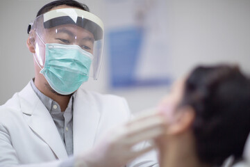 Male dentist wearing face mask, gloves and protective visor shiled as coronavirus safety...
