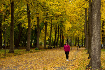 Woman walking alone in the park surrounded by the colorful autumn season trees.