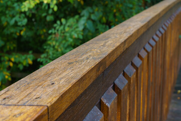 Fototapeta premium Wooden railing of the bridge. The greenery in the background is out of focus. Close-up.