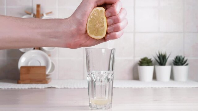 Young man, chef squeezes lemon juice into a glass in the kitchen on the table