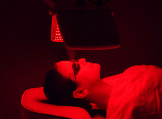 Young woman having red LED light facial therapy treatment in beauty salon. Beauty and wellness - 388945683