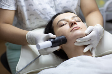 Young woman having facial microcurrent treatment in beauty salon. Beautician using electrical impulses for facial procedure to help serum absorb deep in skin. Healthcare, wellness and medicine