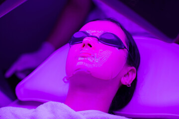 Young woman having purple LED light facial therapy treatment in beauty salon. Beauty and wellness