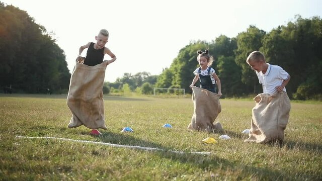 Young kids have fun by playing game by jumping in the bags on field at daytime.