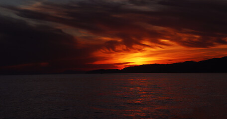 Naklejka na ściany i meble Fotografía de una maravillosa puesta de sol en la playa de Salobreña, Granada. Vemos como el sol crea un precioso cuadro con las nubes y las luces rojas.