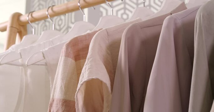 Viewing stylish garments on hangers, closeup. Camera moving backward along wooden clothes rack 