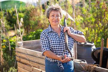 Portrait of retired female amateur gardener posing in homestead with garden equipment