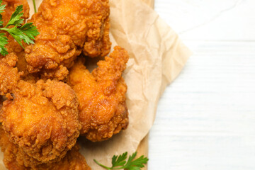 Tasty deep fried chicken pieces on white wooden table, top view. Space for text