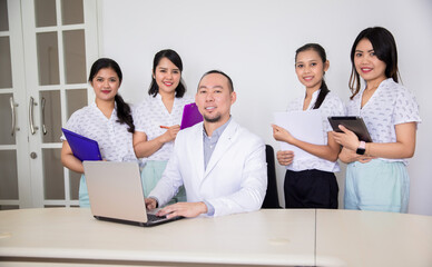 Portrait of confident asian medical team looking at a camera. Female nurses or students standing around male doctor or teacher in clinic office or hospital room