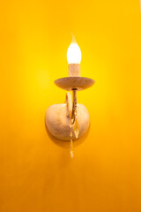 glowing light bulb in the shape of a candle in a beautiful lamp on yellow wall