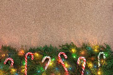 Christmas background with conifer branches, colorful lights and candy canes on a cork board