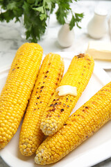 Fresh grilled corn cobs with butter on plate, closeup