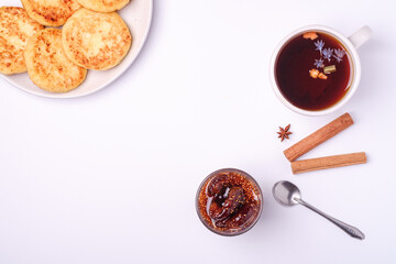 Cottage cheese fritters with fig jam and hot black aromatic tea, Christmas breakfast mood with anise and cinnamon on white background, top view