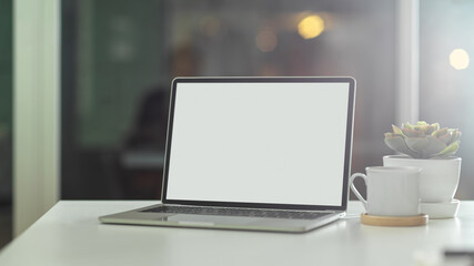 Fototapeta premium White table with laptop, coffee cup and plant pot in office room, clipping path