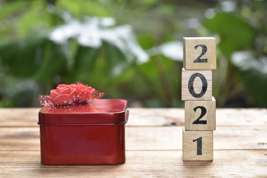 A red gift box and a wooden block with numbers, year 2021.  Placed on a wooden surface