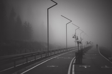 Dark road with double lines disappears into very thick fog and man