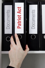 Patriot Act. File Folder is taking by a hand from office shelf. Red Text is on the label of the...