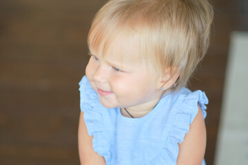 Portrait of a pretty little baby girl in a blue dress. cute blonde babe in the living room