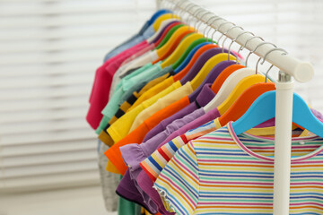 Different child's clothes hanging on rack indoors, closeup