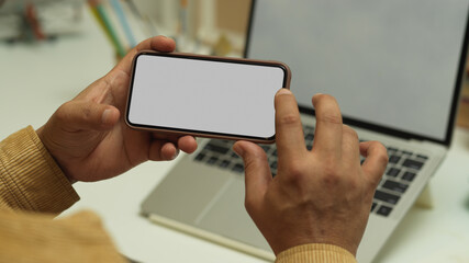 Male hand using horizontal smartphone while sitting in workplace, clipping path