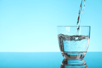 Pouring water into glass on blue background, space for text. Refreshing drink