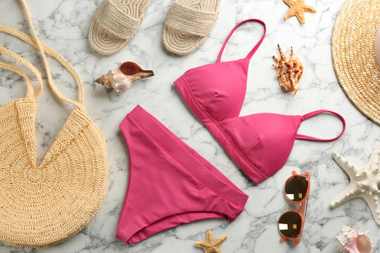Beautiful pink bikini and beach accessories on white marble background, flat lay