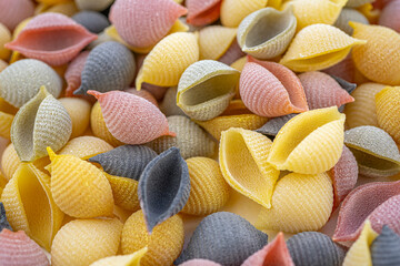 Colored Italian pasta in the shaped of seashells with yellow, pink, and purple colors. Textured background. Macro close up, selective focus.