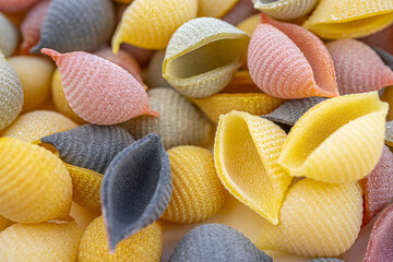 Colored Italian pasta in the shaped of seashells with yellow, pink, and purple colors. Textured background. Macro close up, selective focus.