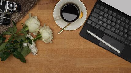 Wooden table with tablet, keyboard, stylus, coffee cup, flower and copy space