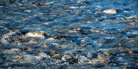 Crystal clear glacial melting water running over smooth rocks and pebbles in a wild forest river. Close up.