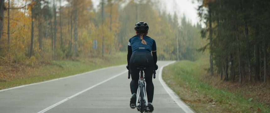 BACK VIEW TRACKING Female cyclist riding her bicycle on an empty forest road in autumn. Shot on RED Cinema camera with 2x Anamorphic lens