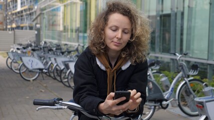 Fototapeta na wymiar Sustainable urban mobility. Young woman checking out bicycle from public transport sharing smartphone app