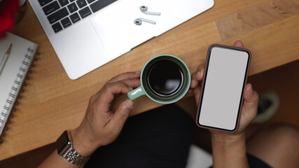 Male hand holding smartphone and coffee cup on workspace, clipping path