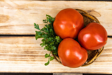 Three tomatoes and parsley in a wicker plate on a wooden background.