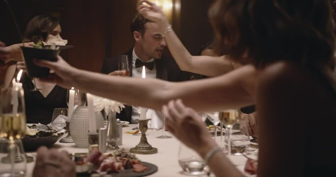 People partying in a restaurant. Multiracial friends sitting together around a table and smiling during gala dinner party.
