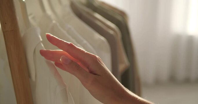 Woman running across garments on clothes rack with hand, closeup