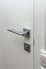 Modern chrome door handle and lock on white wooden door.