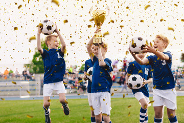 Success of kids football team in tournament final game. Happy boys in school sports team winning soccer championship. Children smiling and rising up golden cup on trophy ceremony