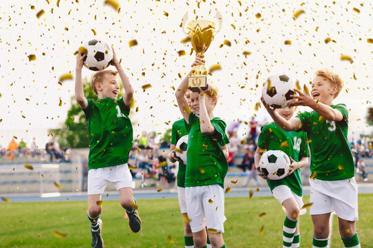 Kids celebrating sports success. Victory of children football team in tournament final game. Happy boys in school sports team winning soccer championship. Children smiling and rising up golden cup