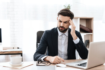 A man sitting at a computer and holding his head.