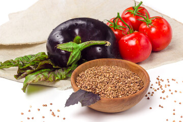 Buckwheat flour in wooden bowl, branch of tomatoes, eggplant on sackcloth isolated on white background. Organic, healthy food concept