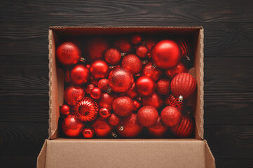 Christmas colored red baubles in a cardboard box on a dark brown wooden background.