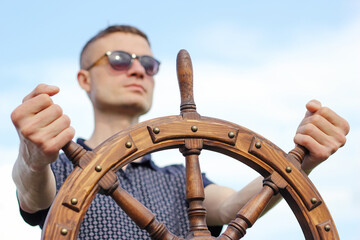 A man controls the yacht, hands on the steering wheel, handwheel on sky background