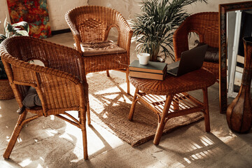 Luxurious and comfortable hotel room in daytime with bamboo chairs and table there are laptop and books with plant on it.