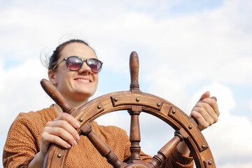 The girl controls the yacht, hands on the steering wheel,  handwheel on sky background