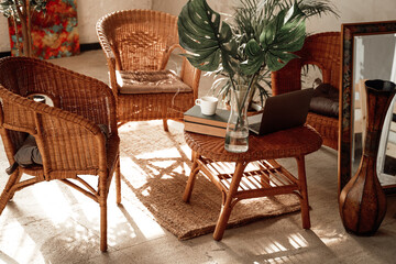 Soft and warm hotel room in daytime with comfortable bamboo furniture and table there are books with cup and laptop.